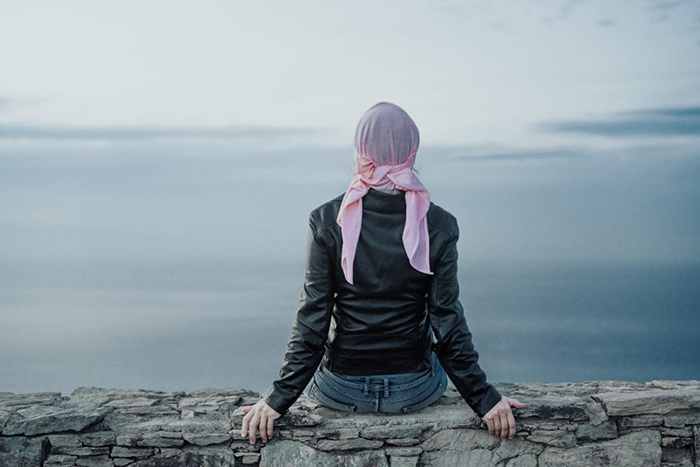 woman sits on beach wearing pink head scarf