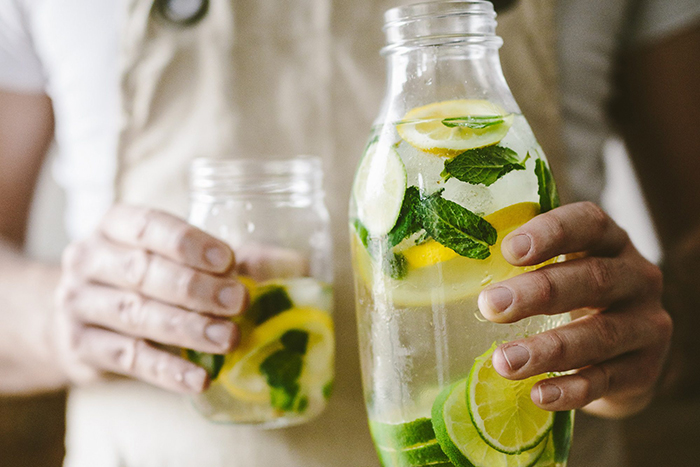 a jug of water with lemons, limes, and mint