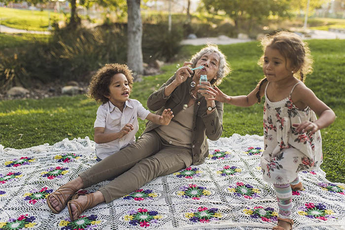 elderly woman blows bubbles with grandchildren in park