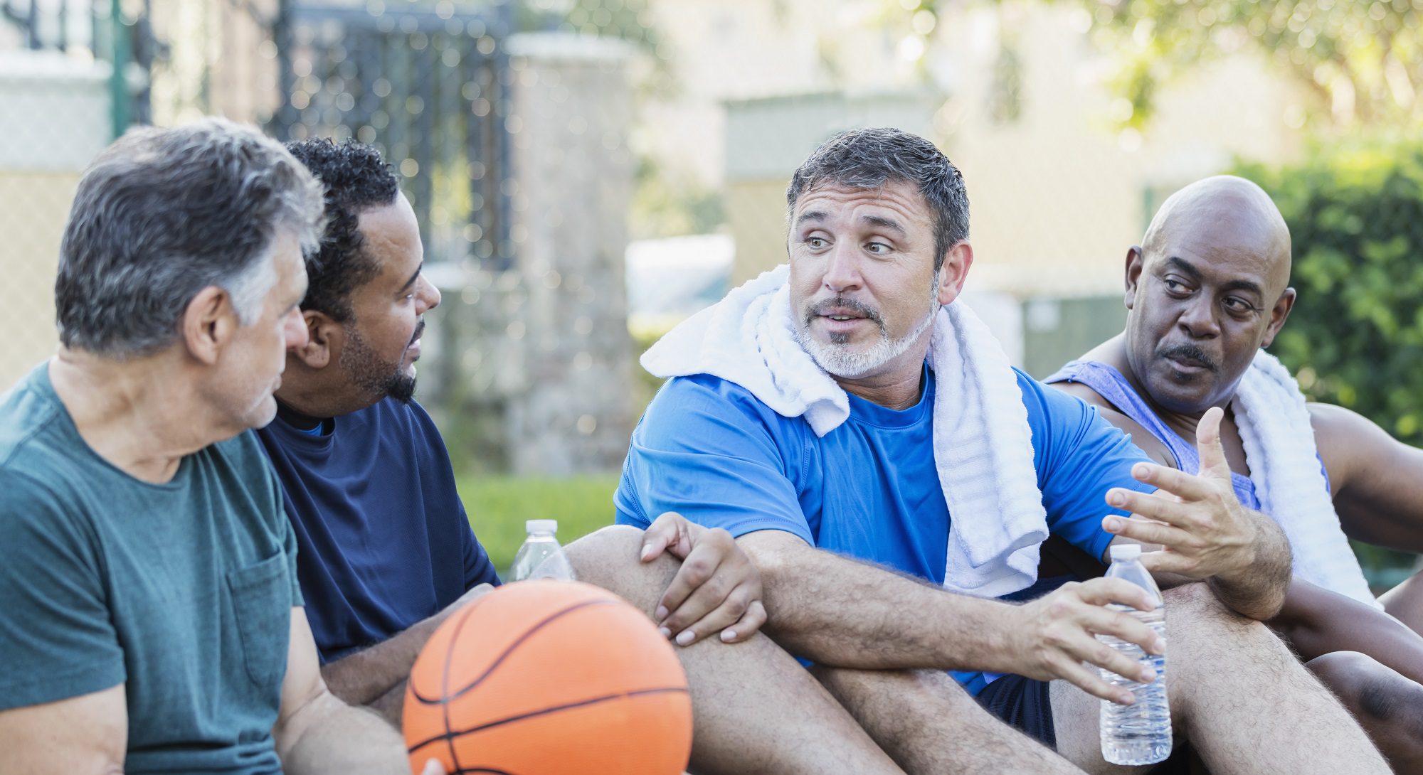 four men sitting with a basketball and drinking water
