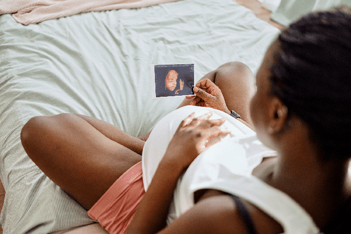 expectant mother rests her  hand on her  belly while looking at an ultrasound photo of her  baby