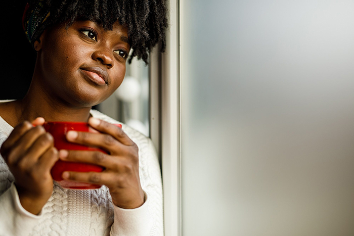 woman gazes out the window while holding a mug