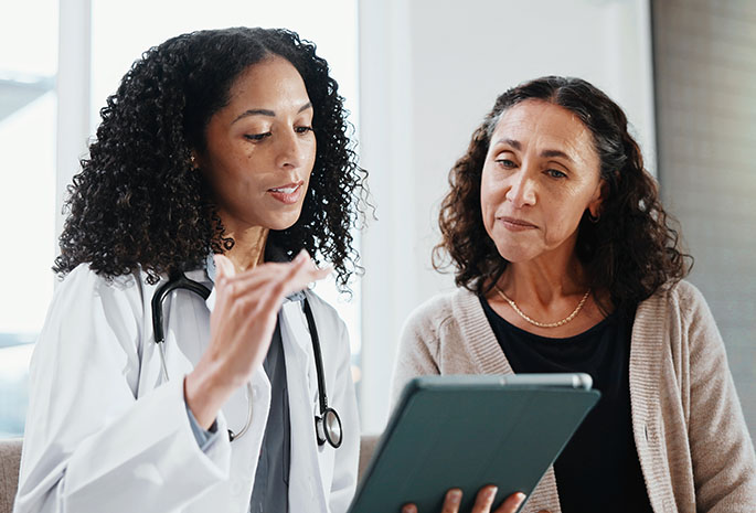 female physician speaking with female patient while sharing on her hand-held device